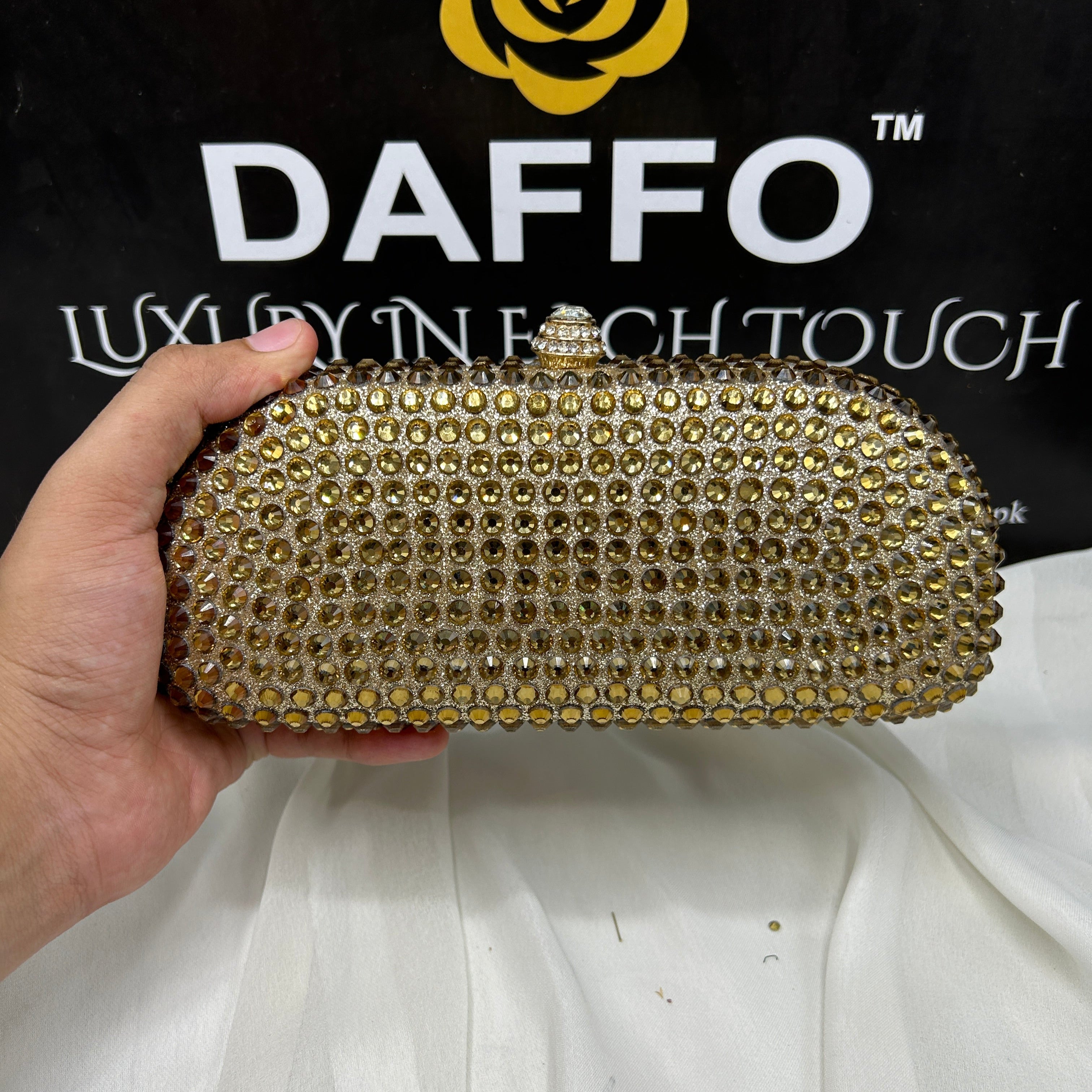 Gold clutch held by a hand with 'DAFFO' logo in the background